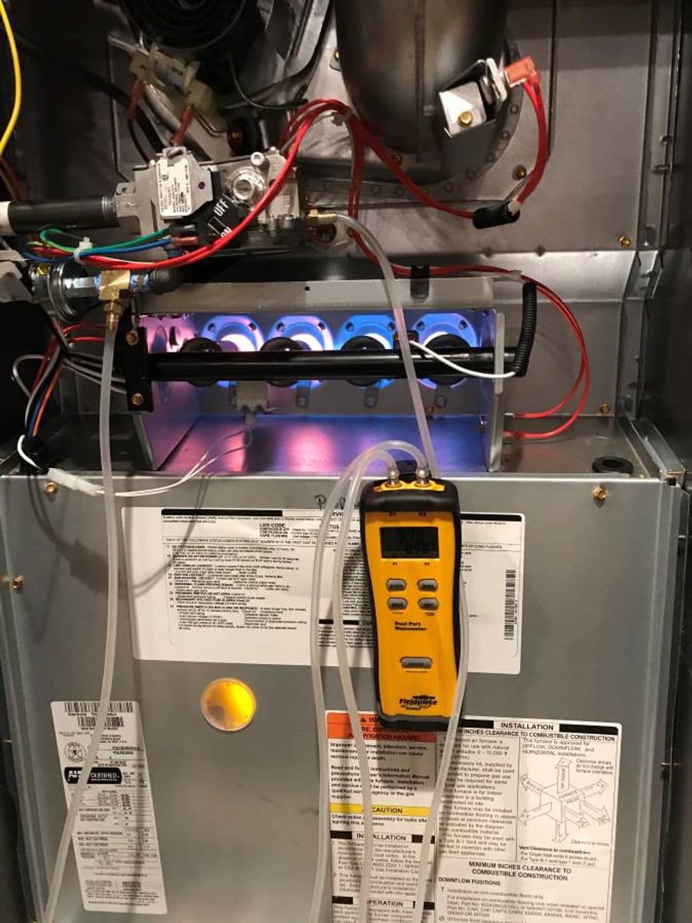 Gas furnace interior showing ignition system, sensors, and multimeter for diagnostics.