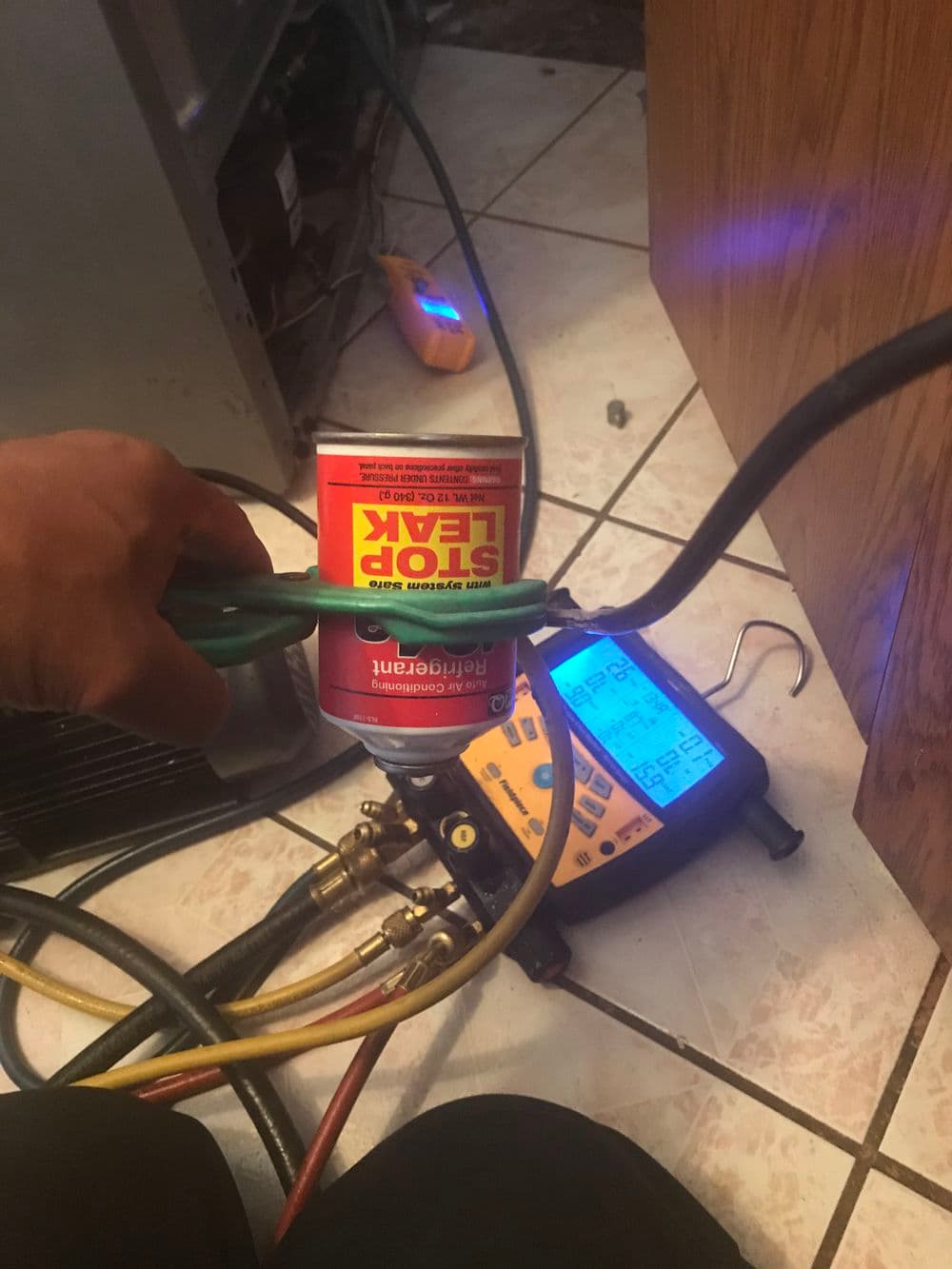 Hand holding Stop Leak can near HVAC gauges and tools on tiled floor.